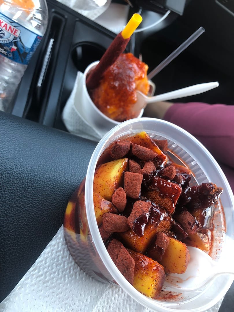 Two cups of mango and chili snacks, one with a tamarind candy straw, in a car.