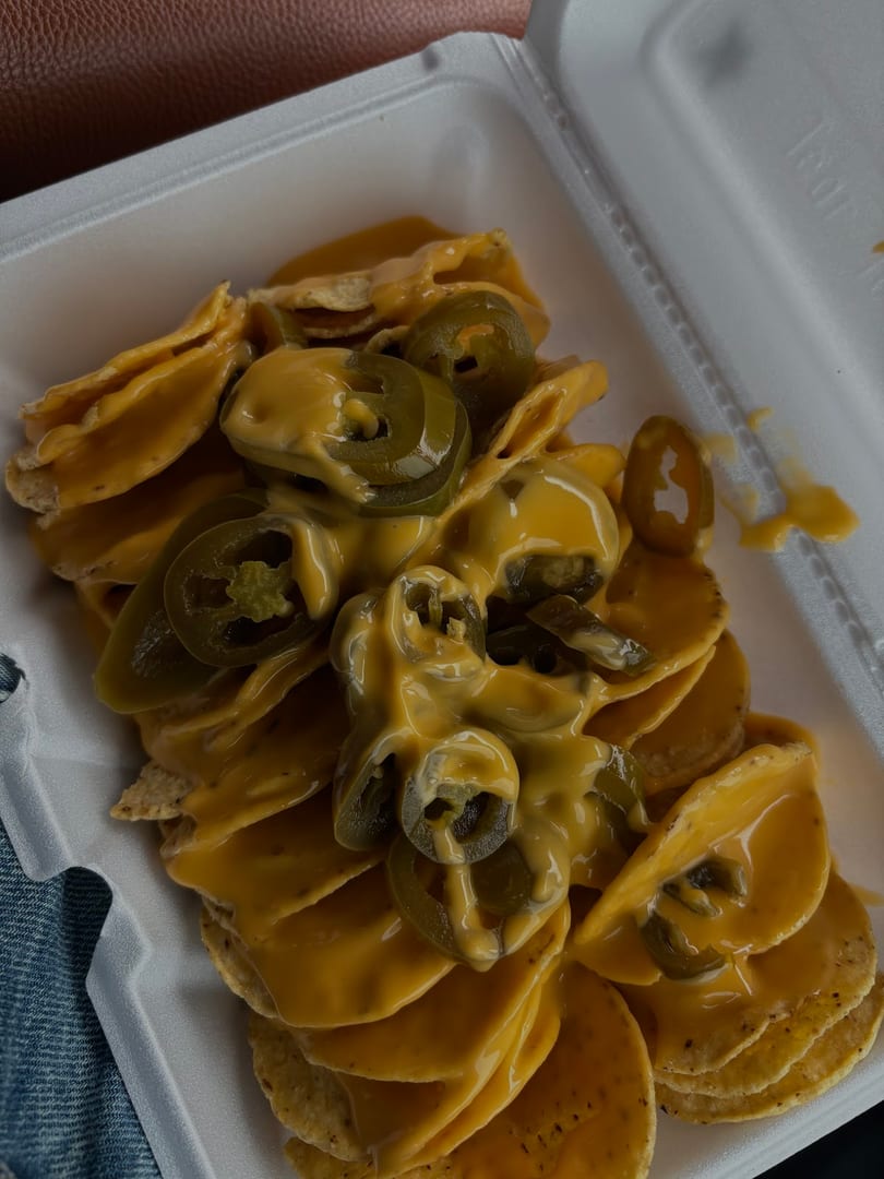 Nachos with melted cheese and sliced jalapeños in a white takeout container.