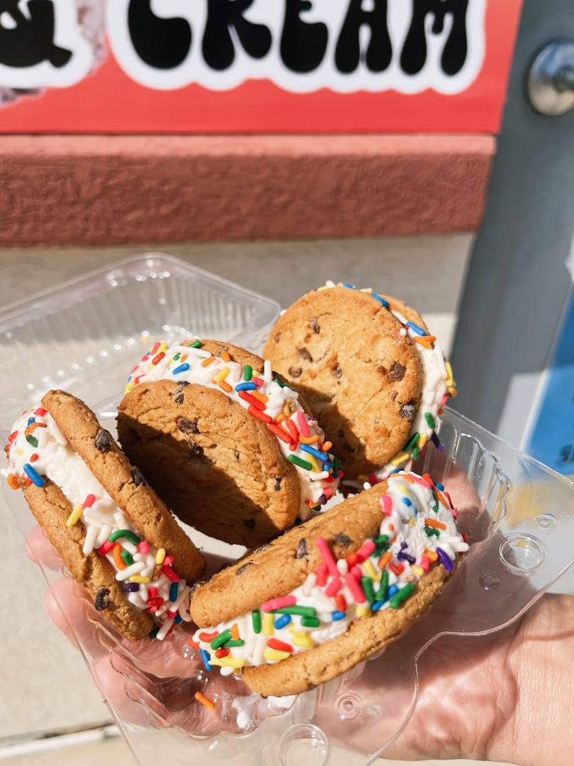 Four chocolate chip cookie ice cream sandwiches with colorful sprinkles in a plastic container.