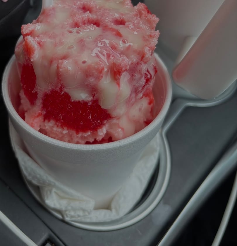 A white cup filled with red and pink shaved ice, drizzled with condensed milk.